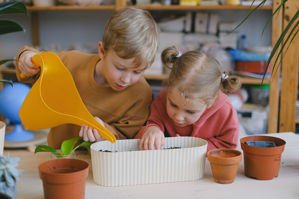 Two children planting seeds in pots indoors, learning about gardening and nature